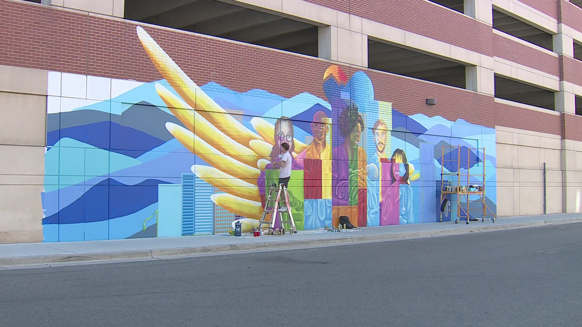 Artist Austin Zucchini-Fowler is working on a mural at the entrance to the outpatient medical center parking garage off Acoma Street.