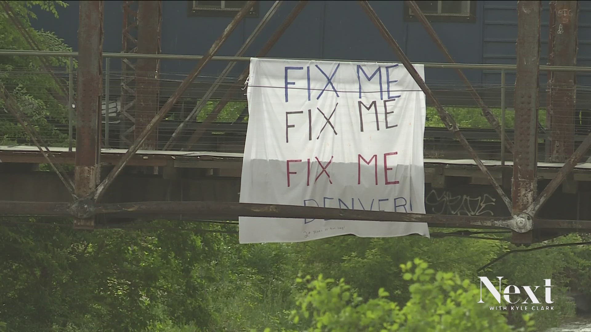 Someone hung a cloth sign from the steel of an old railroad bridge where Delgany Street dead ends next to the creek. It reads: “Fix Me, Fix Me, Fix Me Denver.”