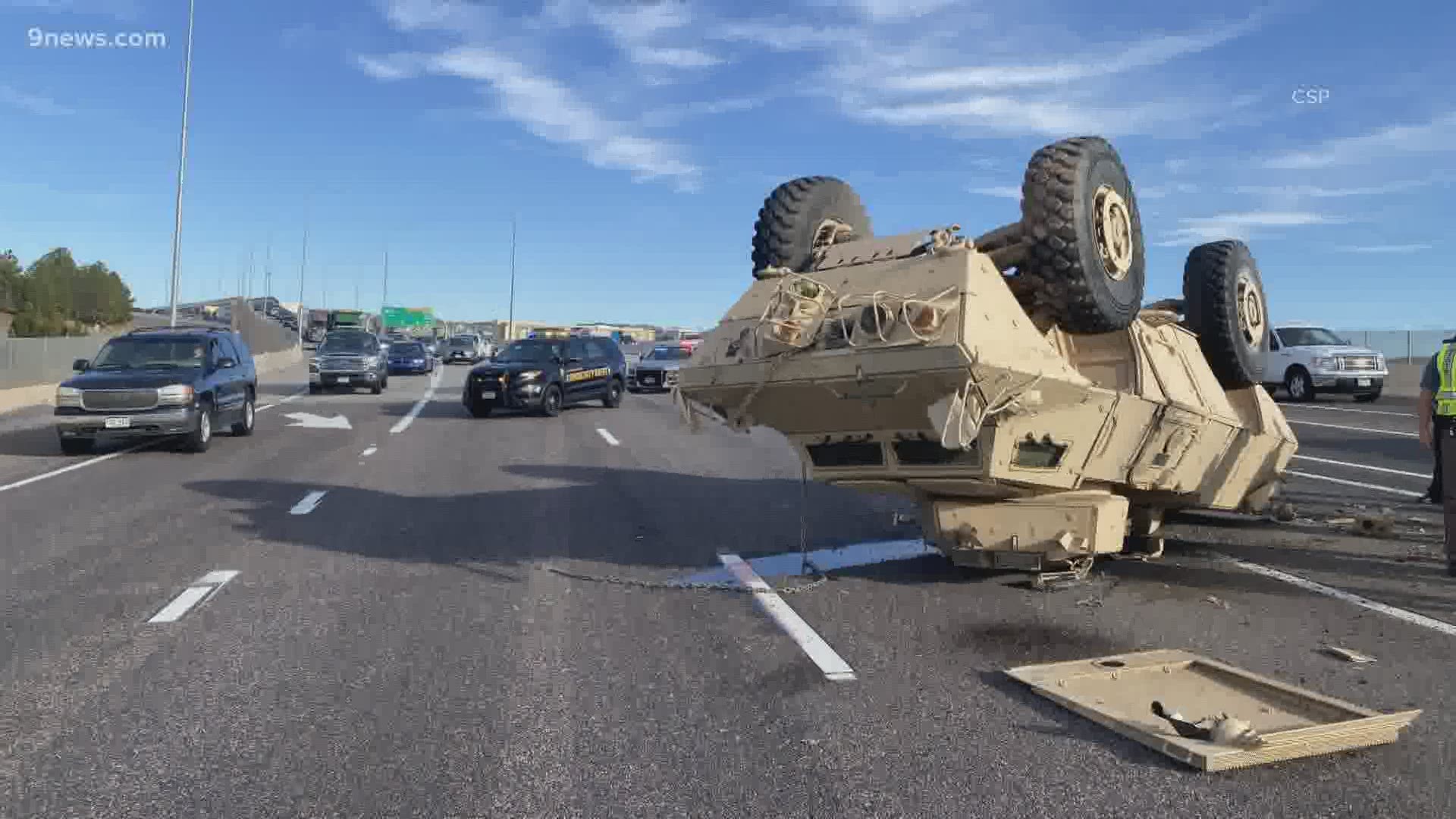 An armored military carrier fell off a semi-truck and landed upside down in the middle of the road.